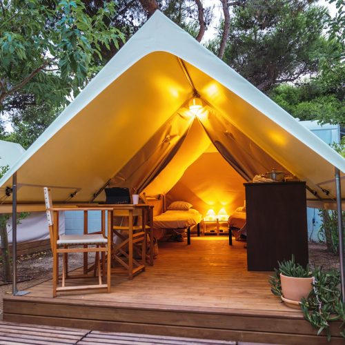 Cozy open glamping tent with light inside during dusk. Luxury camping tent